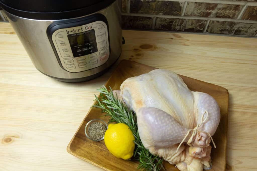 Raw whole chicken on a plate with aromatics next to an Instant Pot pressure cooker.