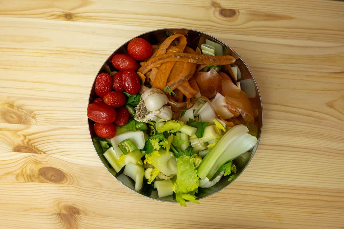 Bowl with cherry tomatoes, carrot peels, chopping celery, garlic, and onions