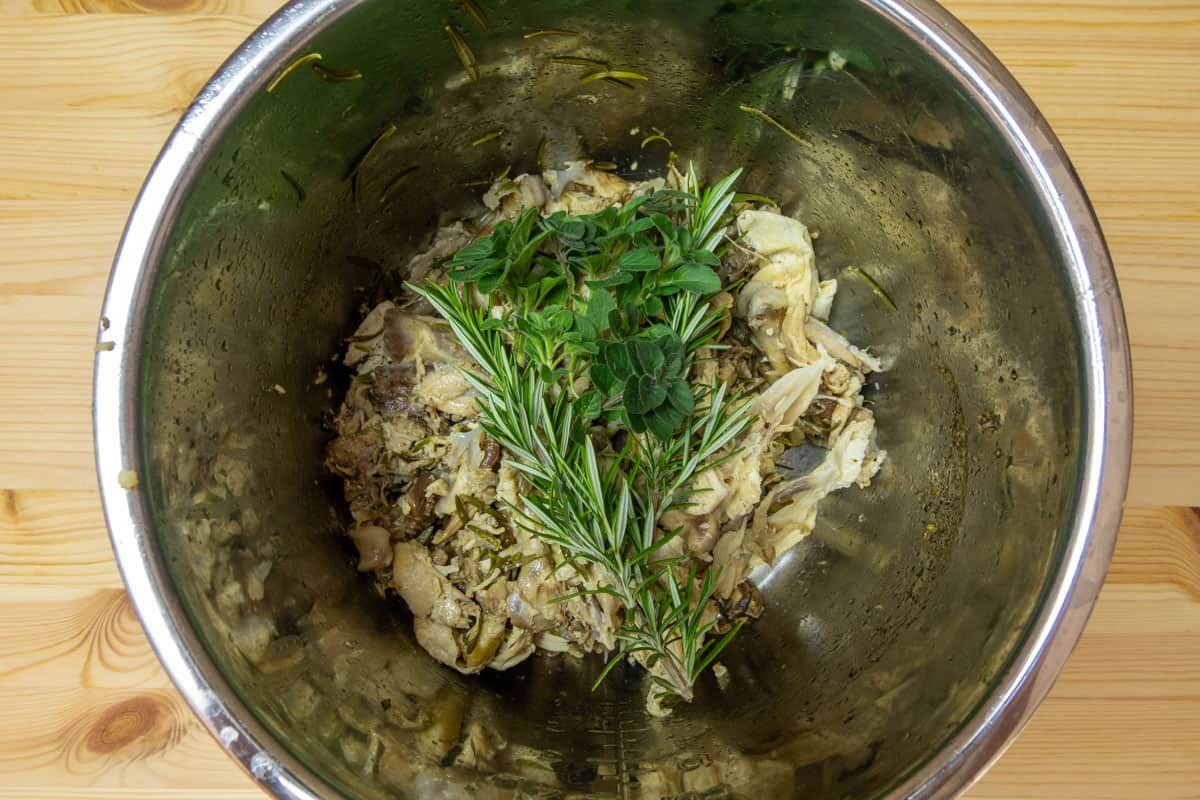 Instant Pot inner pot with chicken bones, rosemary, and thyme