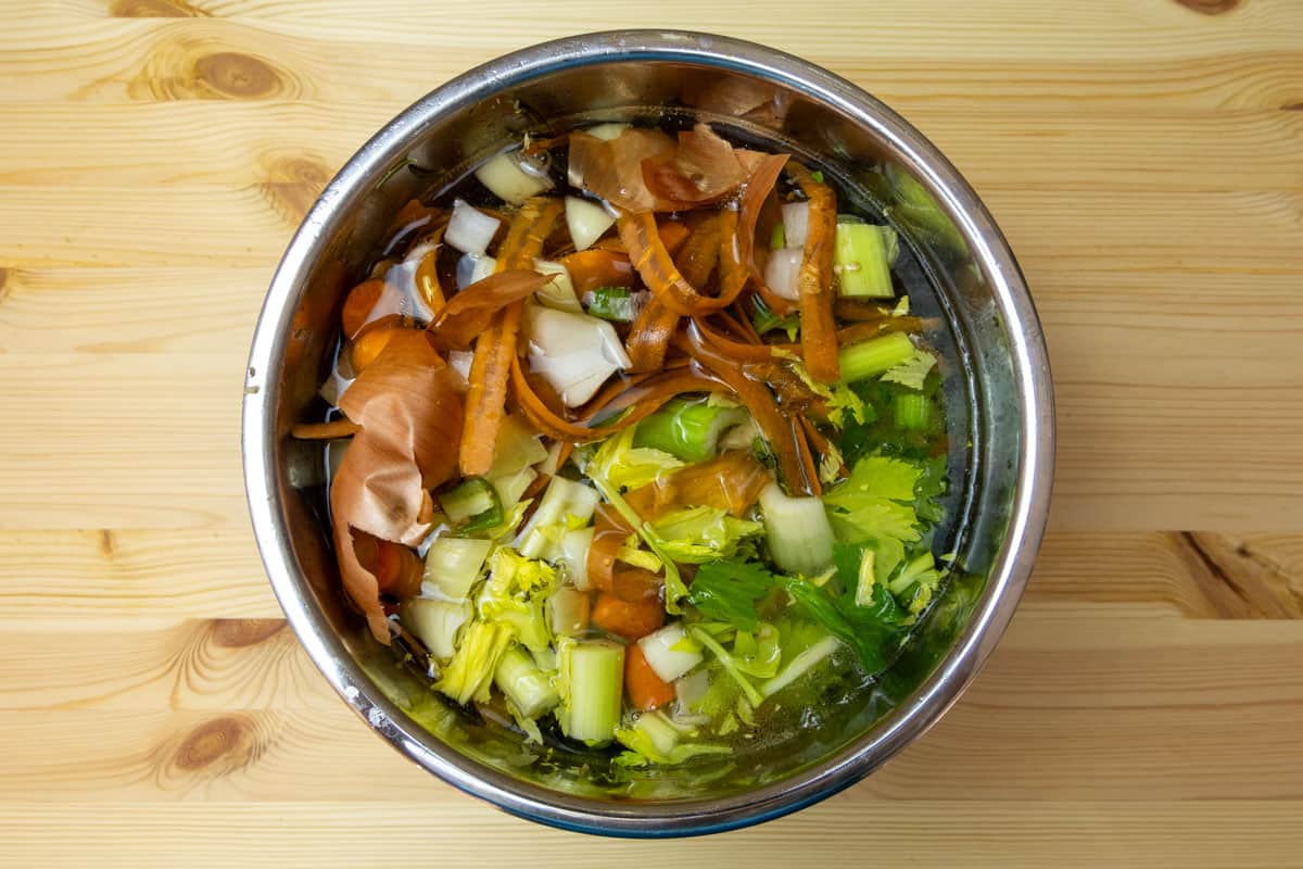 Instant Pot inner pot with vegetable scraps, chicken bones, and water