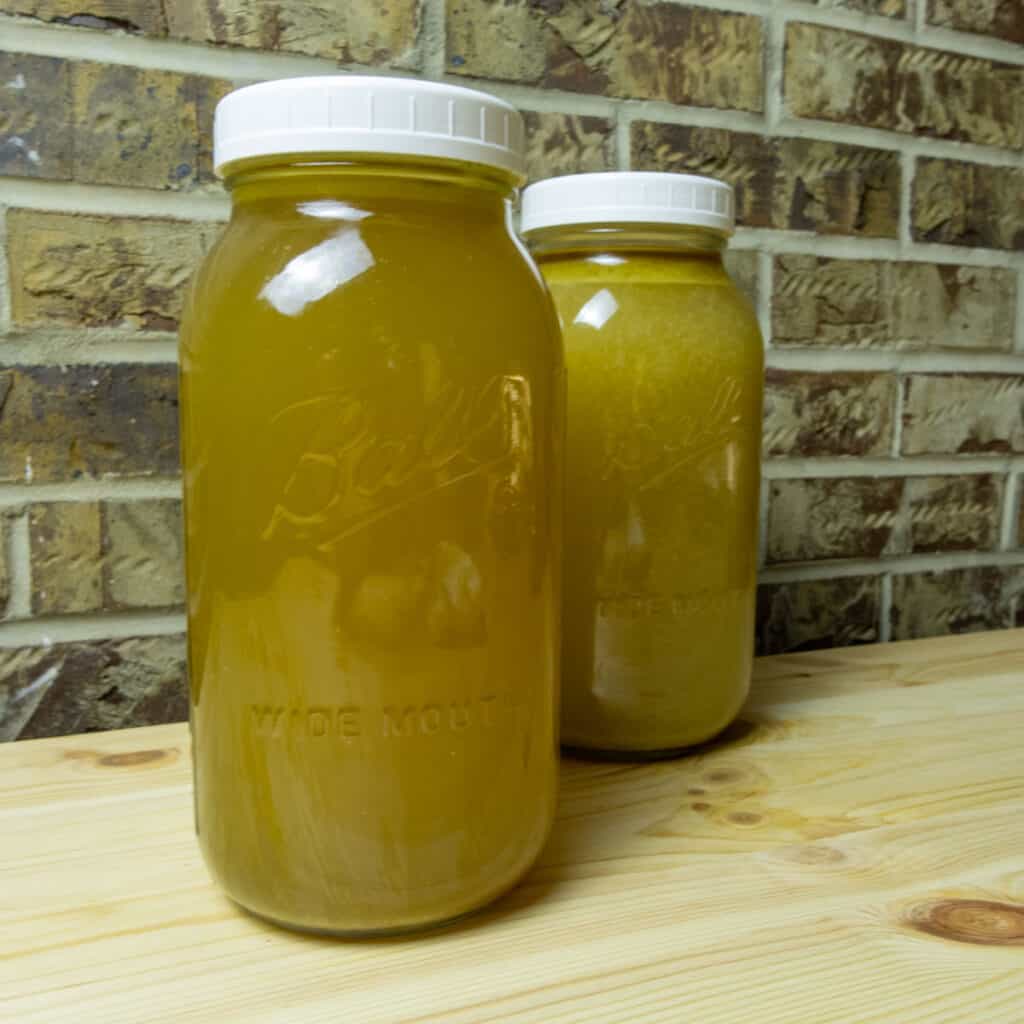 Two half gallon mason jars filled with golden chicken stock.