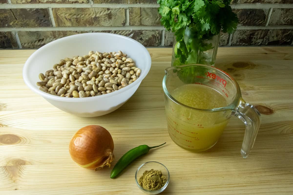 Ingredients to make refried beans including beans, chicken stock, cilantro, serrano pepper, onion, and cumin