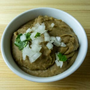 A white bowl with refried beans with white onion and cilantro on top.