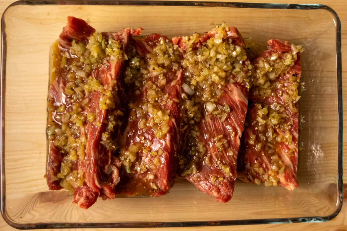Flap meat in a dish with marinade including white onion, garlic, soy sauce, and lime juice on top.
