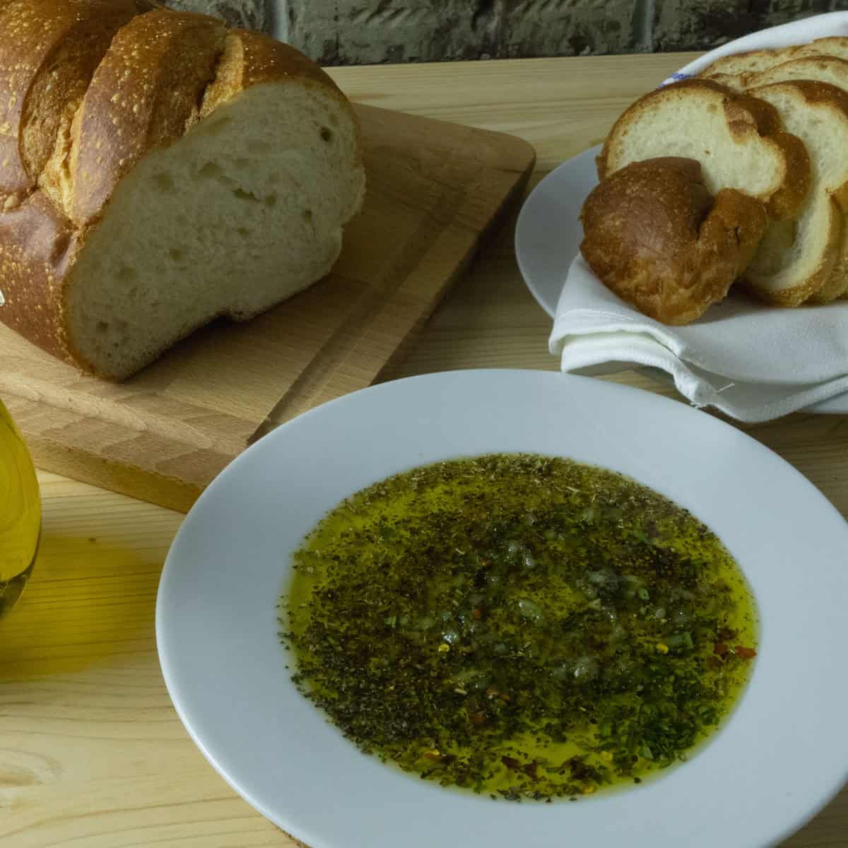 Olive oil bread dip on a plate with a loaf of bread and sliced bread in the background.