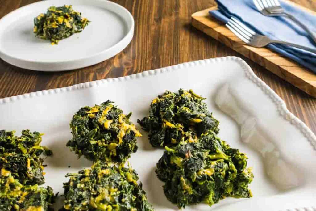 Four spinach squares on a white platter with a plated spinach square in the back with forks.
