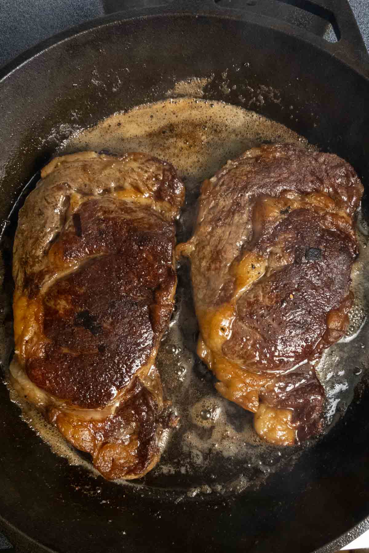 Two steaks in a cast iron after they've been cooked on one side.