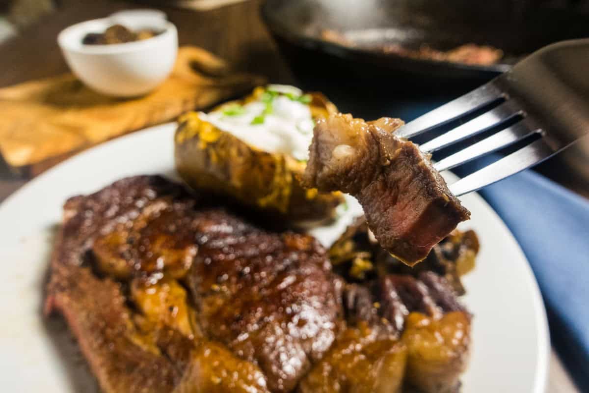 Steak on a plate with a fork and bite of medium rare steak.