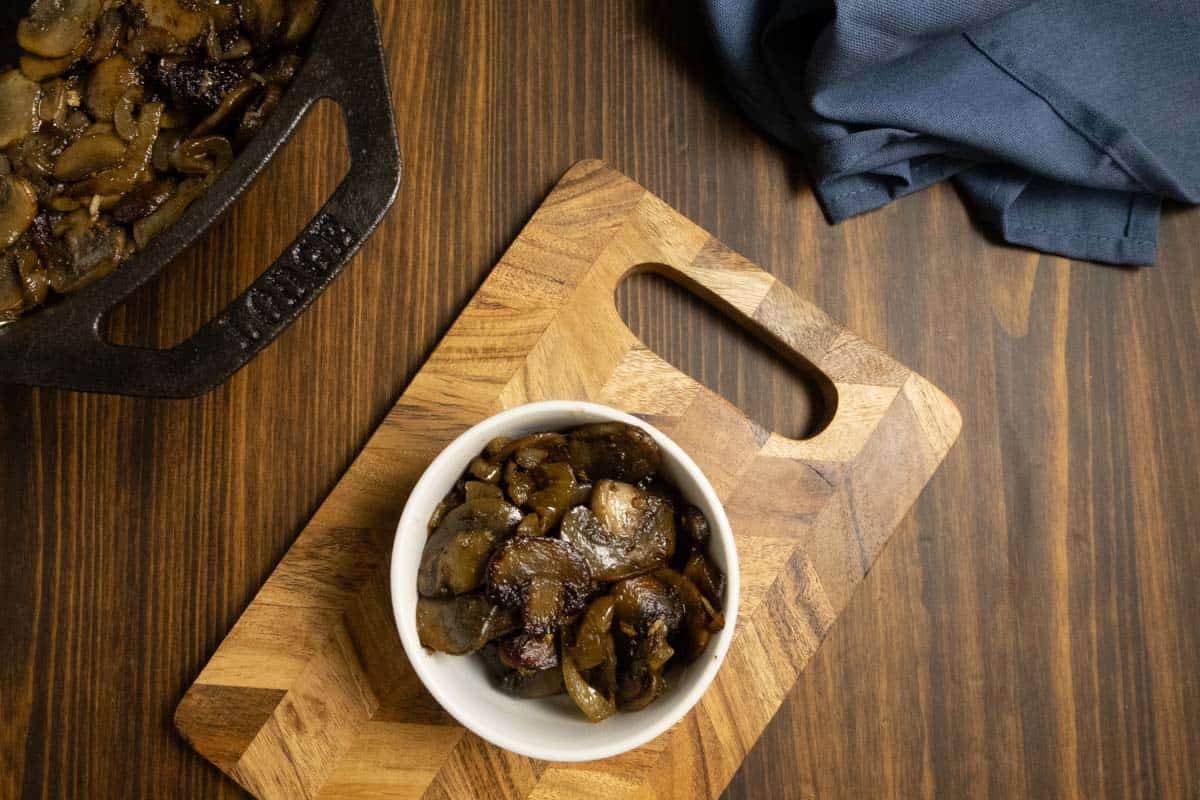 Mushrooms and onions in a bowl on a cutting board.