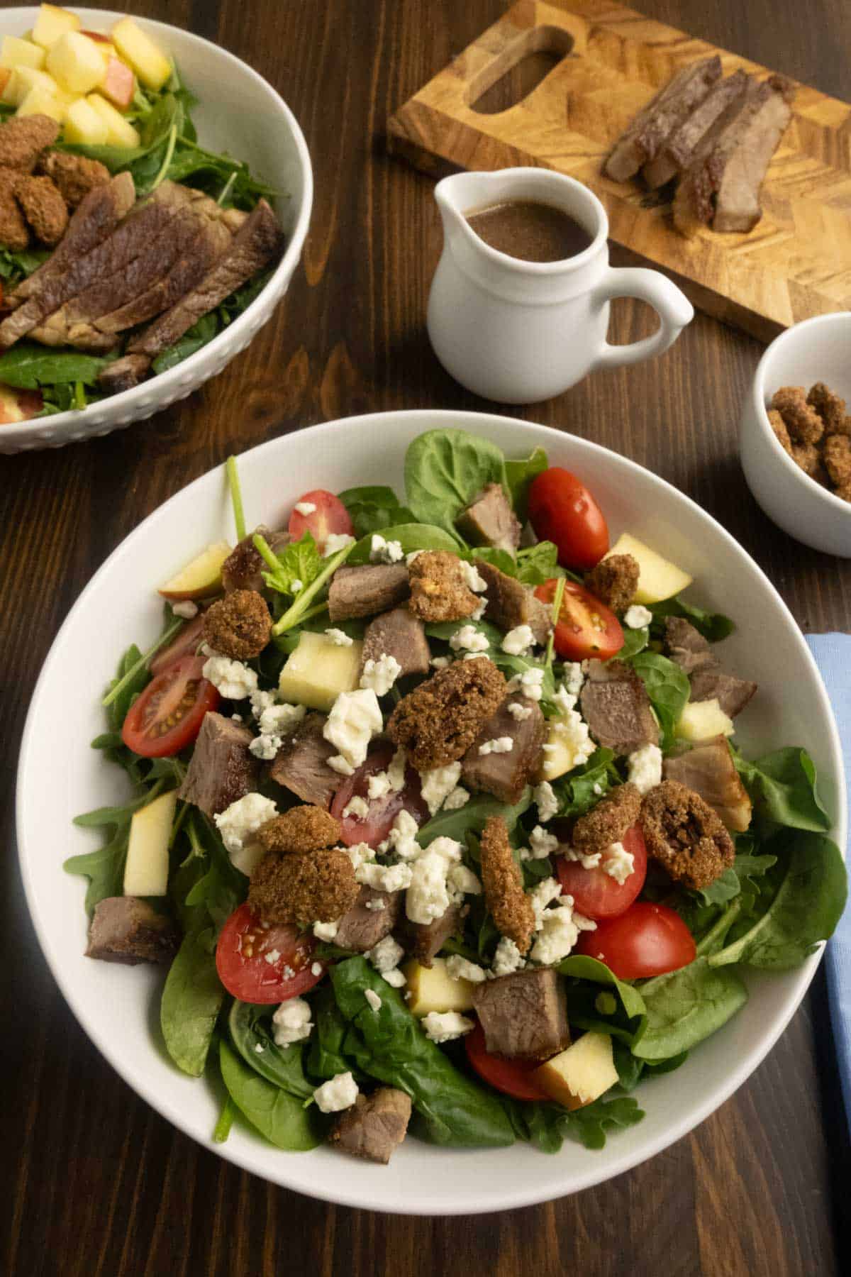 Arugula and spinach salad with steak and apples mixed together in a salad bowl.
