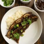 Flanken Beef Ribs on a plate with Coconut Rice with cilantro, green onions, and sauce.