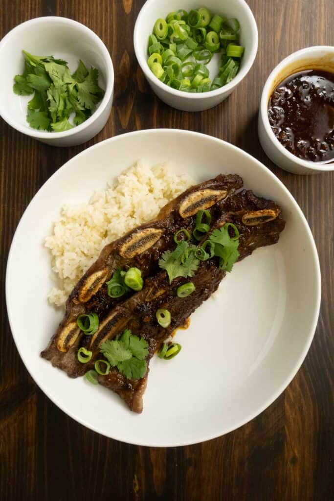 Flanken Beef Ribs on a plate with Coconut Rice with cilantro, green onions, and sauce.