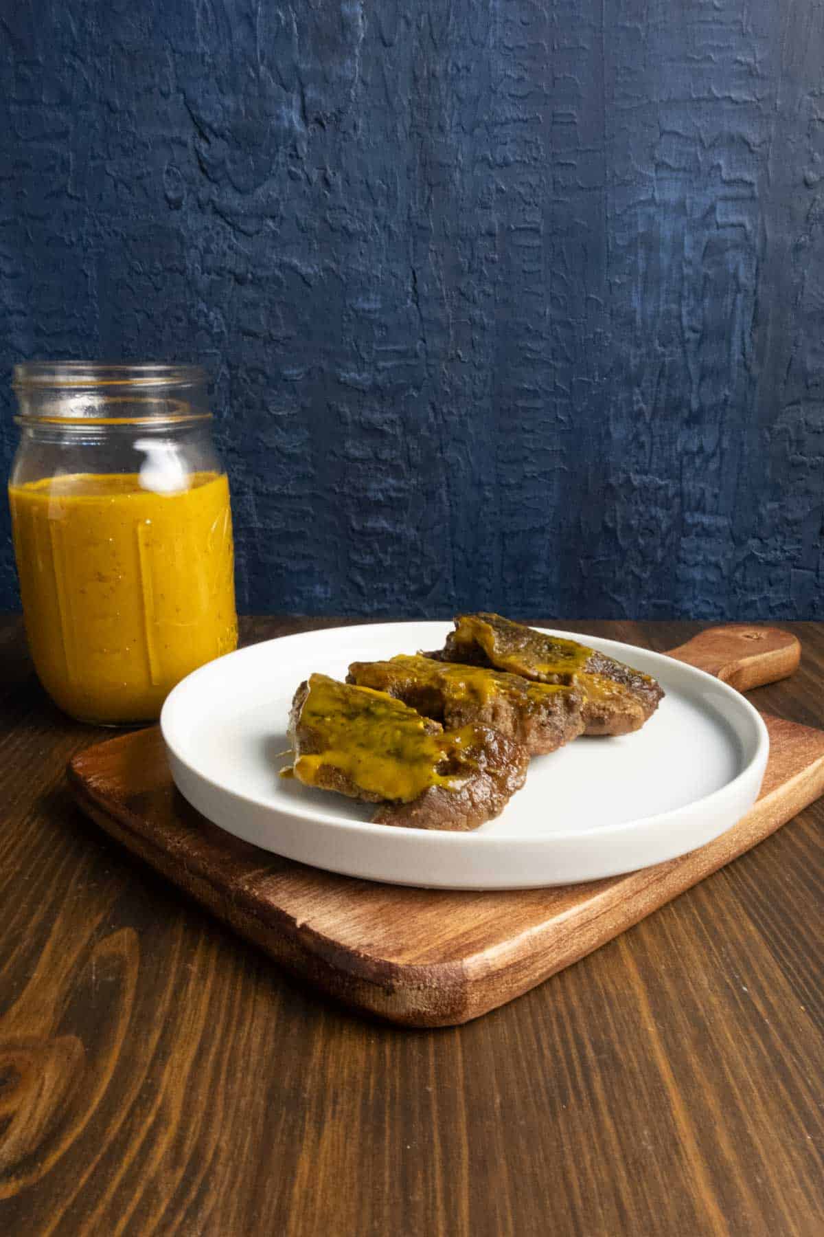 Boneless beef ribs on a plate with Carolina mustard BBQ sauce on them.