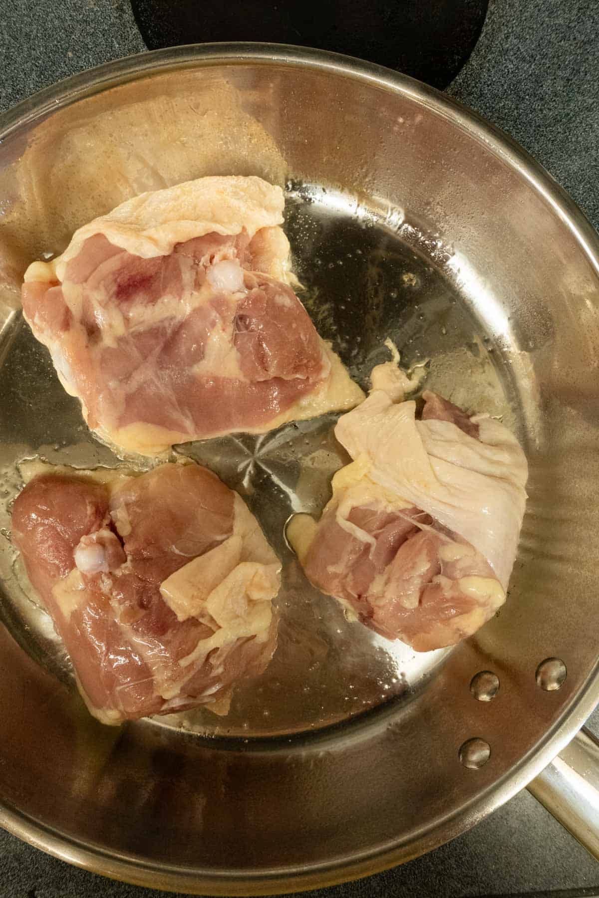 Chicken thighs skin side down on a skillet.