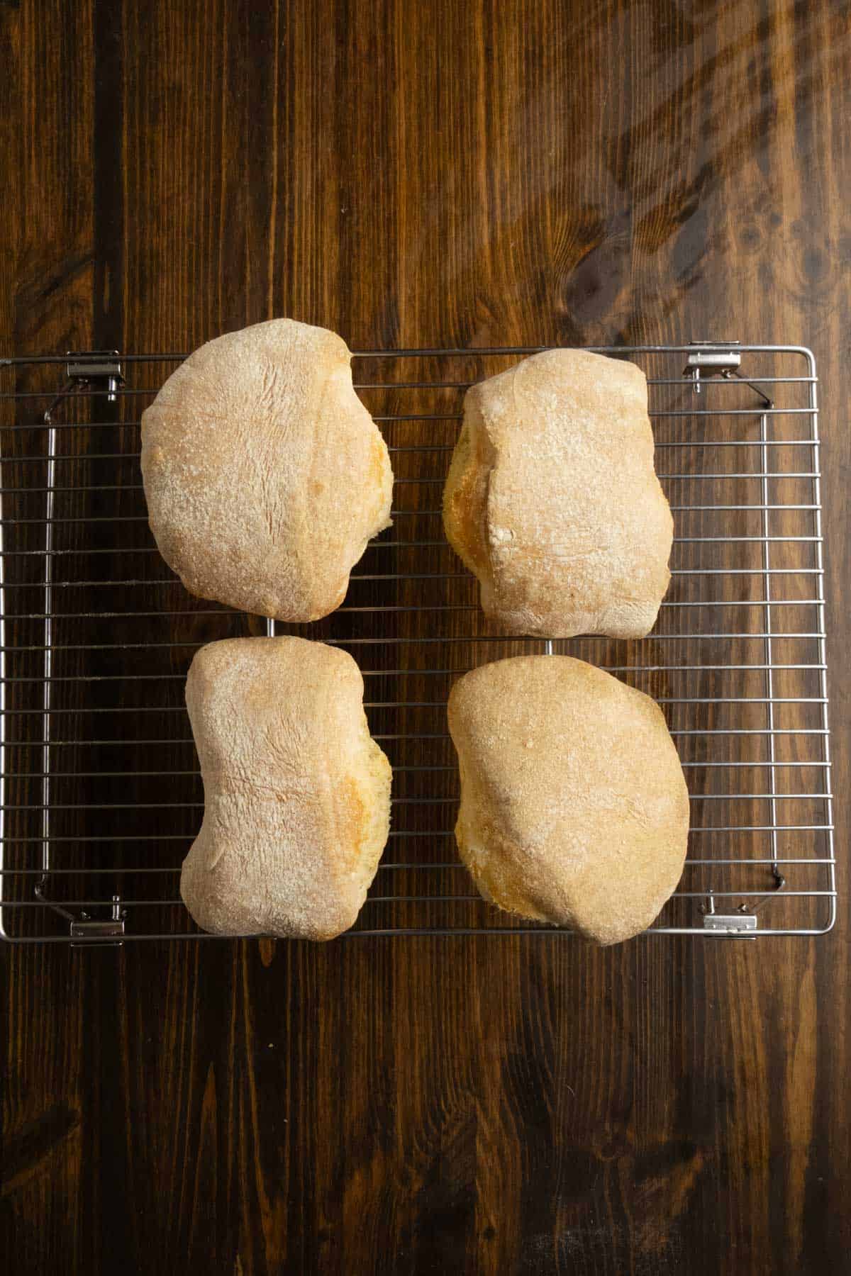 Ciabatta rolls on a wire cooling rack.