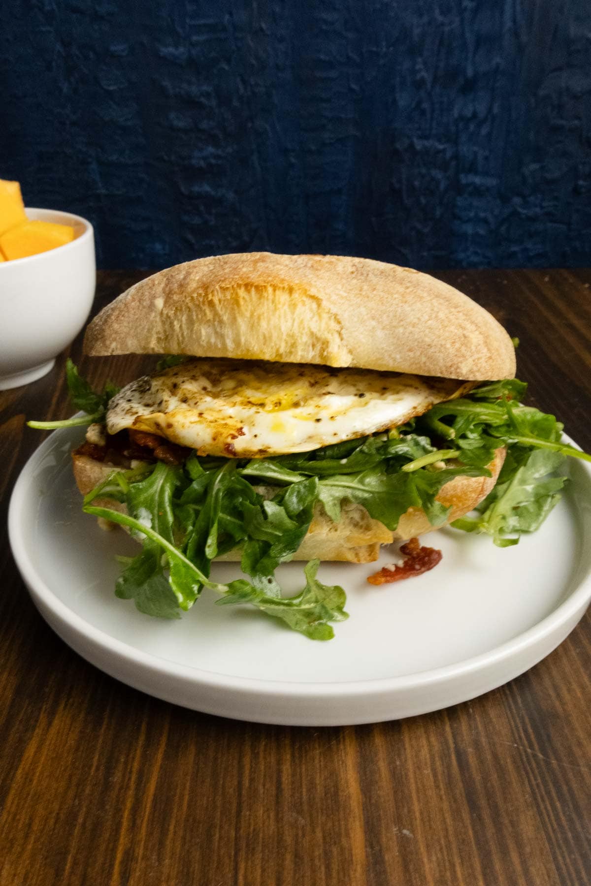 Finished egg sandwich with arugula and bacon spilling out.