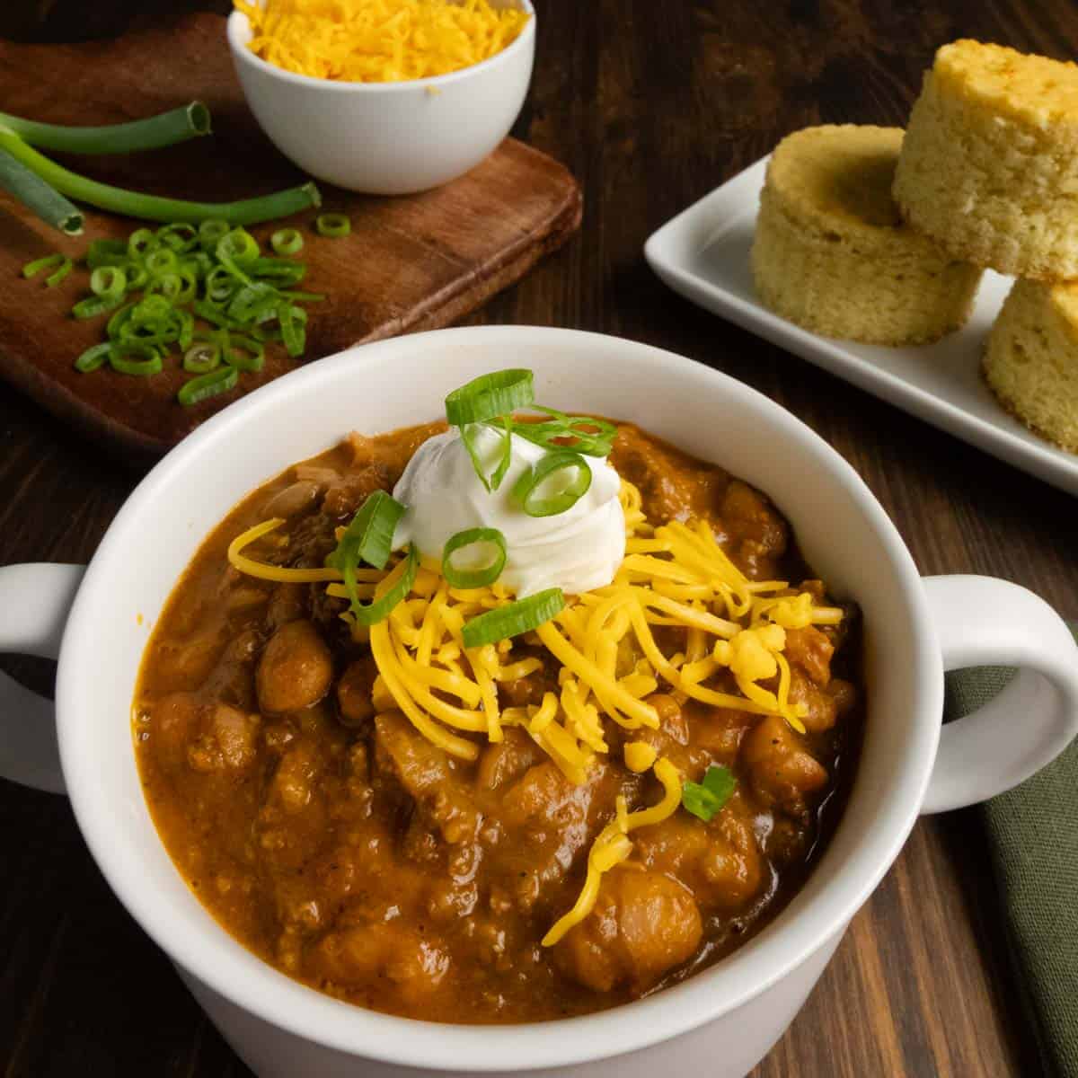 Close up of a bowl of chili with cheese, green onions, and sour cream.