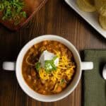 Bowl of chili with green onion, cheddar cheese, and sour cream.