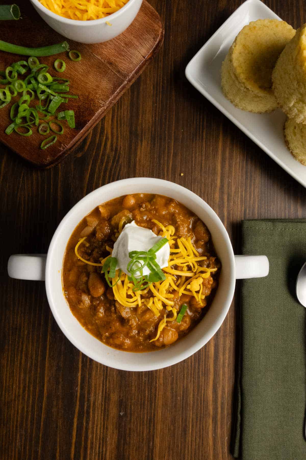 Bowl of chili with green onion, cheddar cheese, and sour cream.