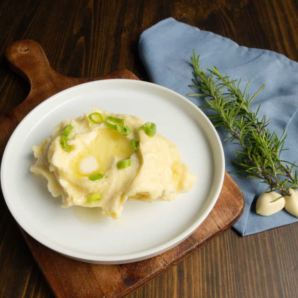Rosemary garlic mashed potatoes on a plate with rosemary sprigs and garlic on the side.
