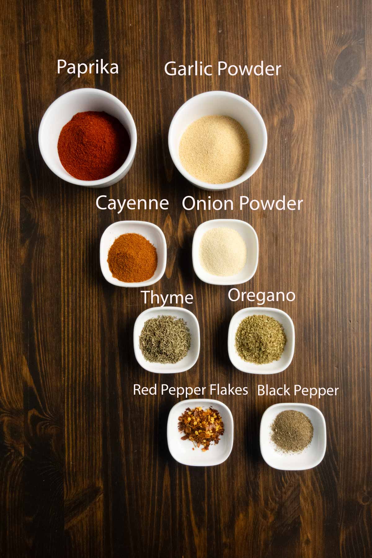 Ingredient photo with paprika, garlic powder, onion powder, cayenne, thyme, oregano, red pepper flakes, and black pepper.