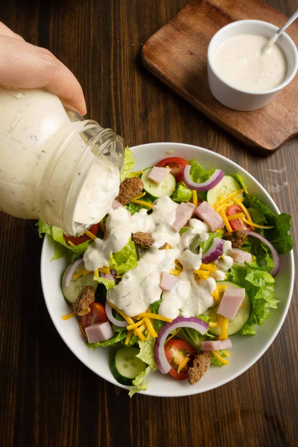 Mason jar of herby ranch dressing being poured onto a salad.