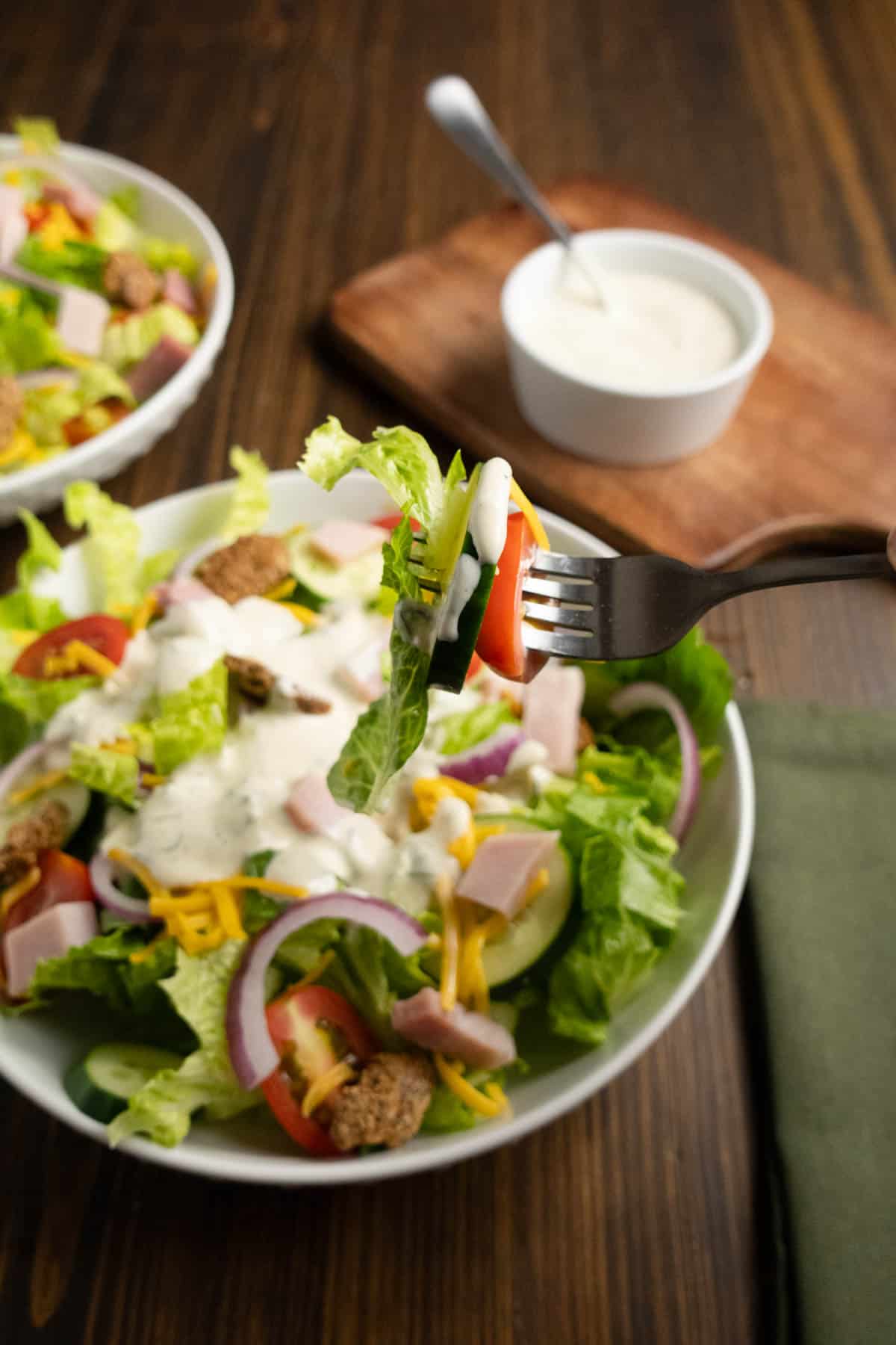 A fork with a bite of salad on it with ranch dressing.