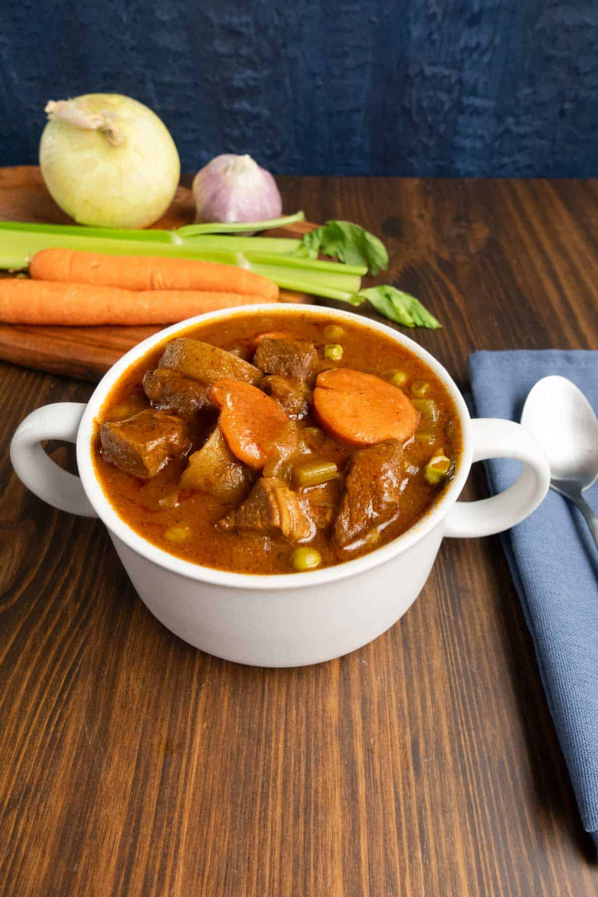 Bowl of stovetop beef stew closeup with mirepoix vegetables in the background.