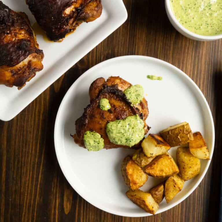 A plate of Peruvian chicken thighs with green sauce and roasted potatoes.
