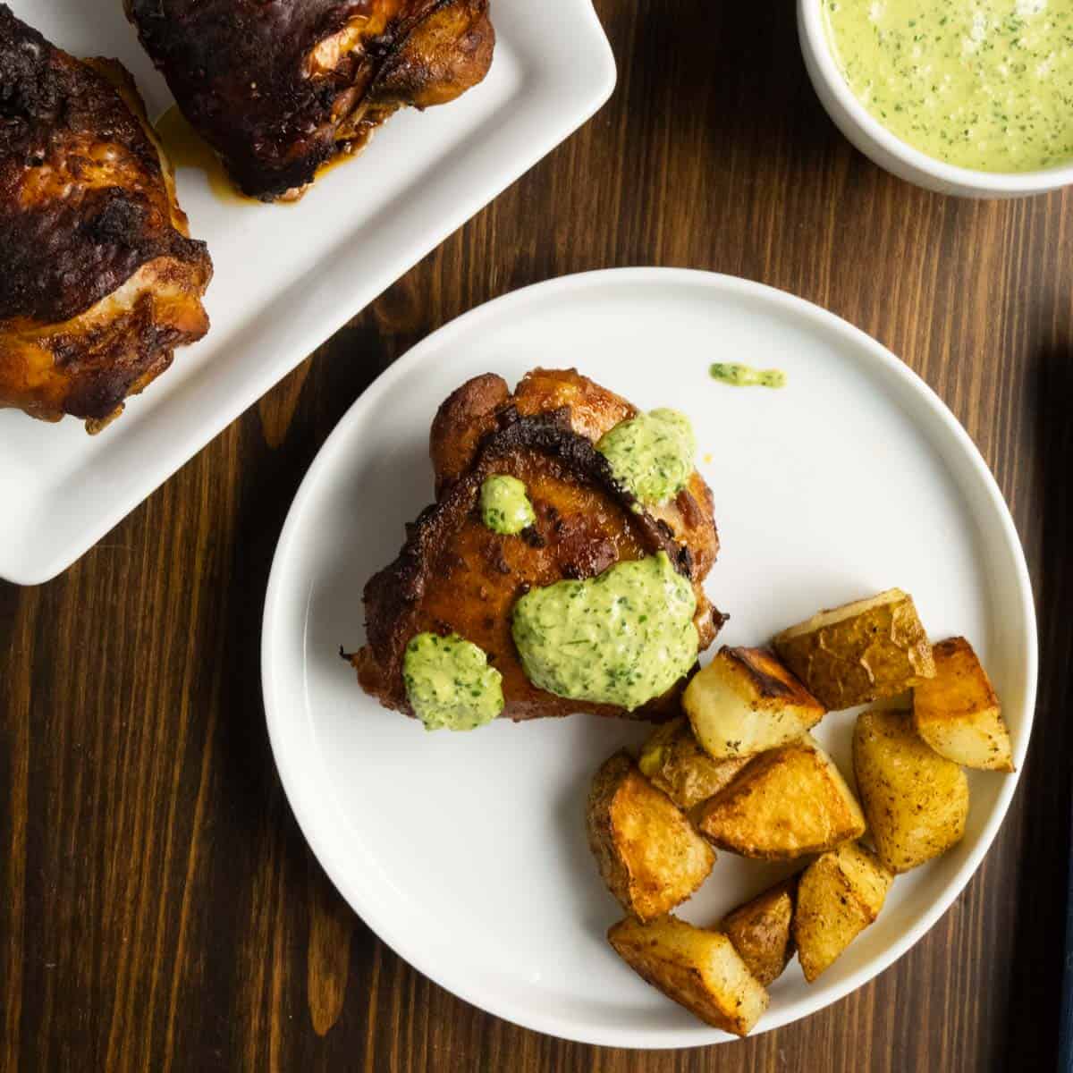 A plate of Peruvian chicken thighs with green sauce and roasted potatoes.