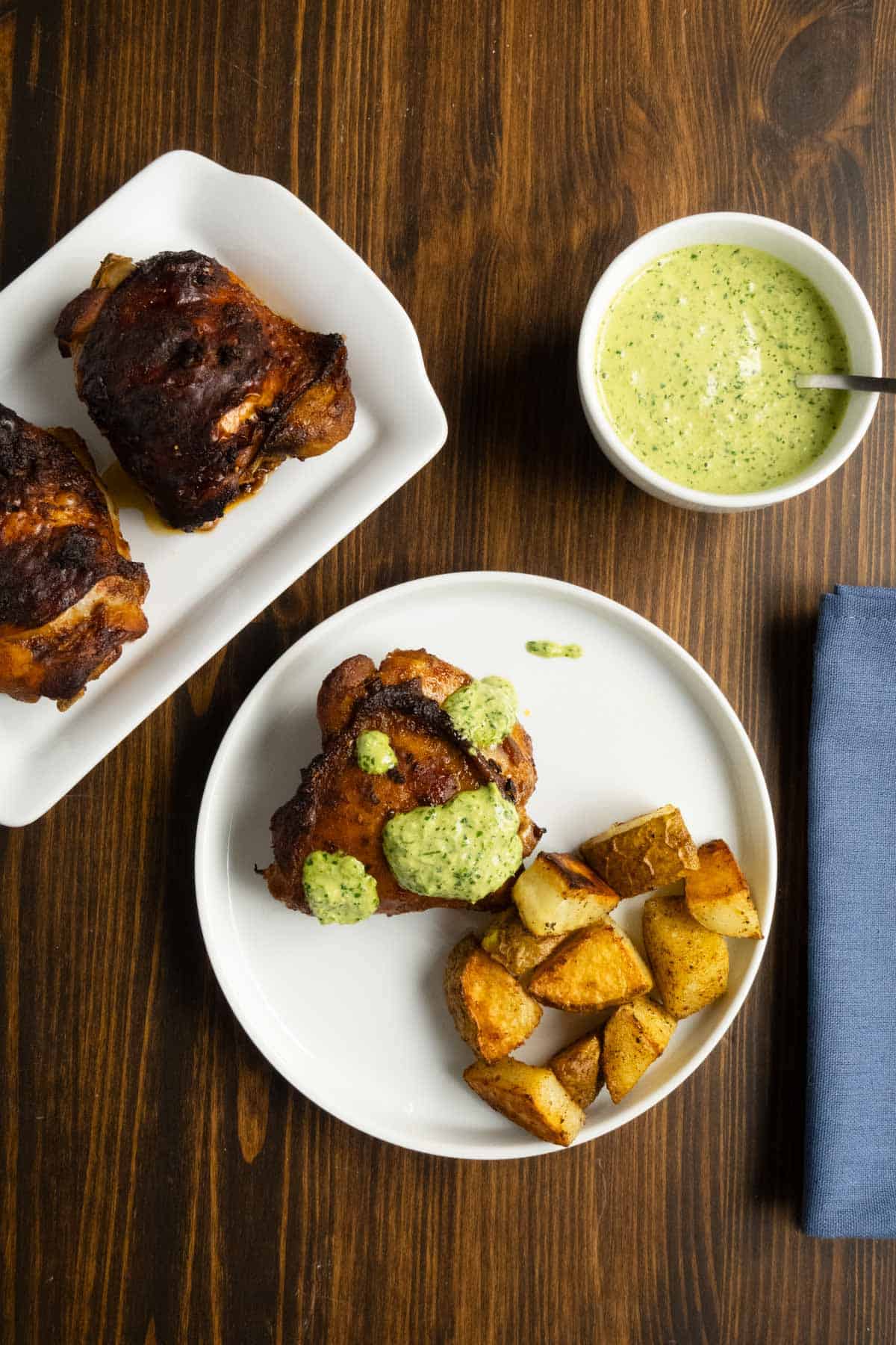 A plate with a Peruvian chicken thigh and green sauce with roasted potatoes.