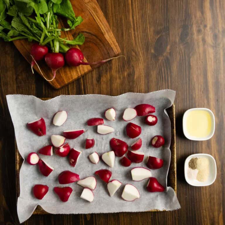 A tray of raw radishes on a baking tray with oil and seasonings on the side.