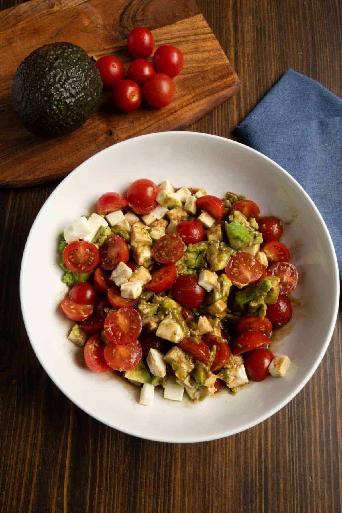 Bowl of tomato, avocado, mozzarella salad with an avocado and cherry tomatoes in the back.