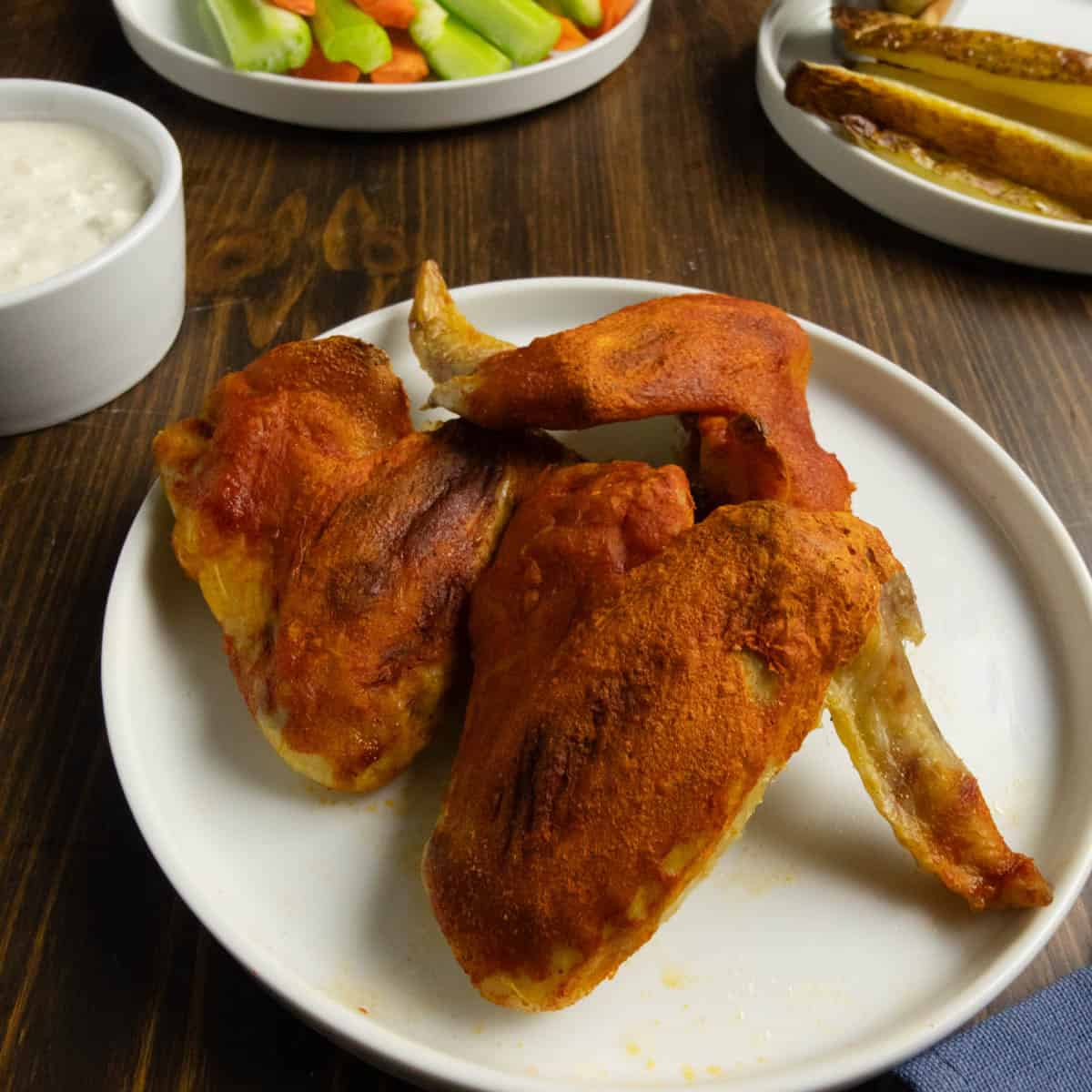 Close up on crispy baked chicken wings with Buffalo sauce with blue cheese dressing, oven baked fries, and celery and carrots in the background.