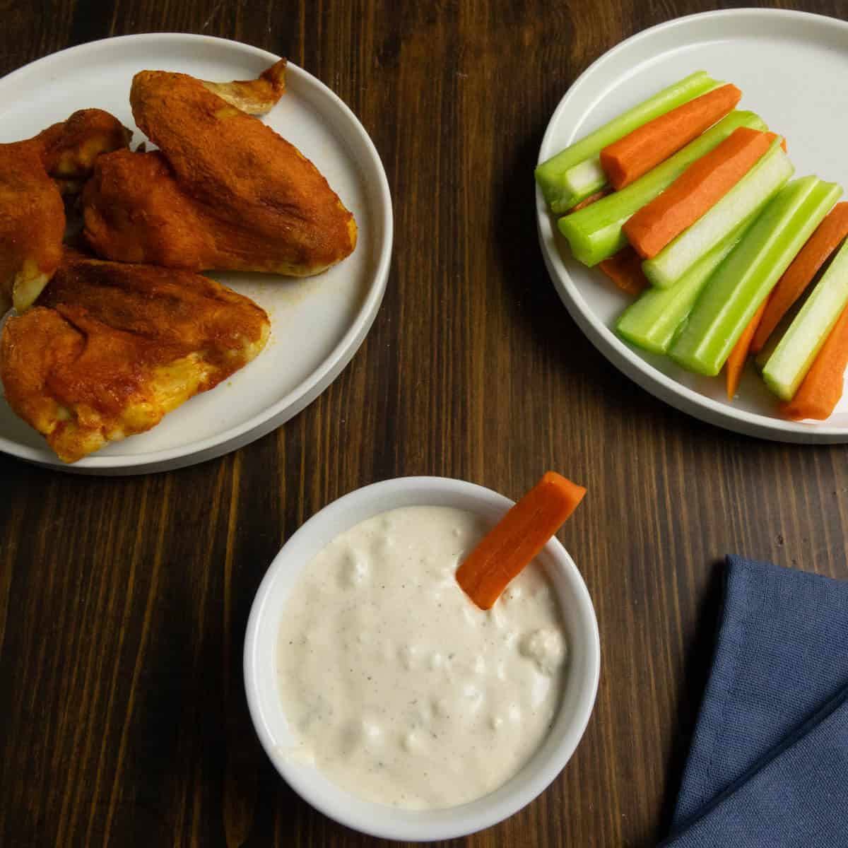 Overhead shot of blue cheese dressing in a bowl with baked chicken wings and vegetables on the side.