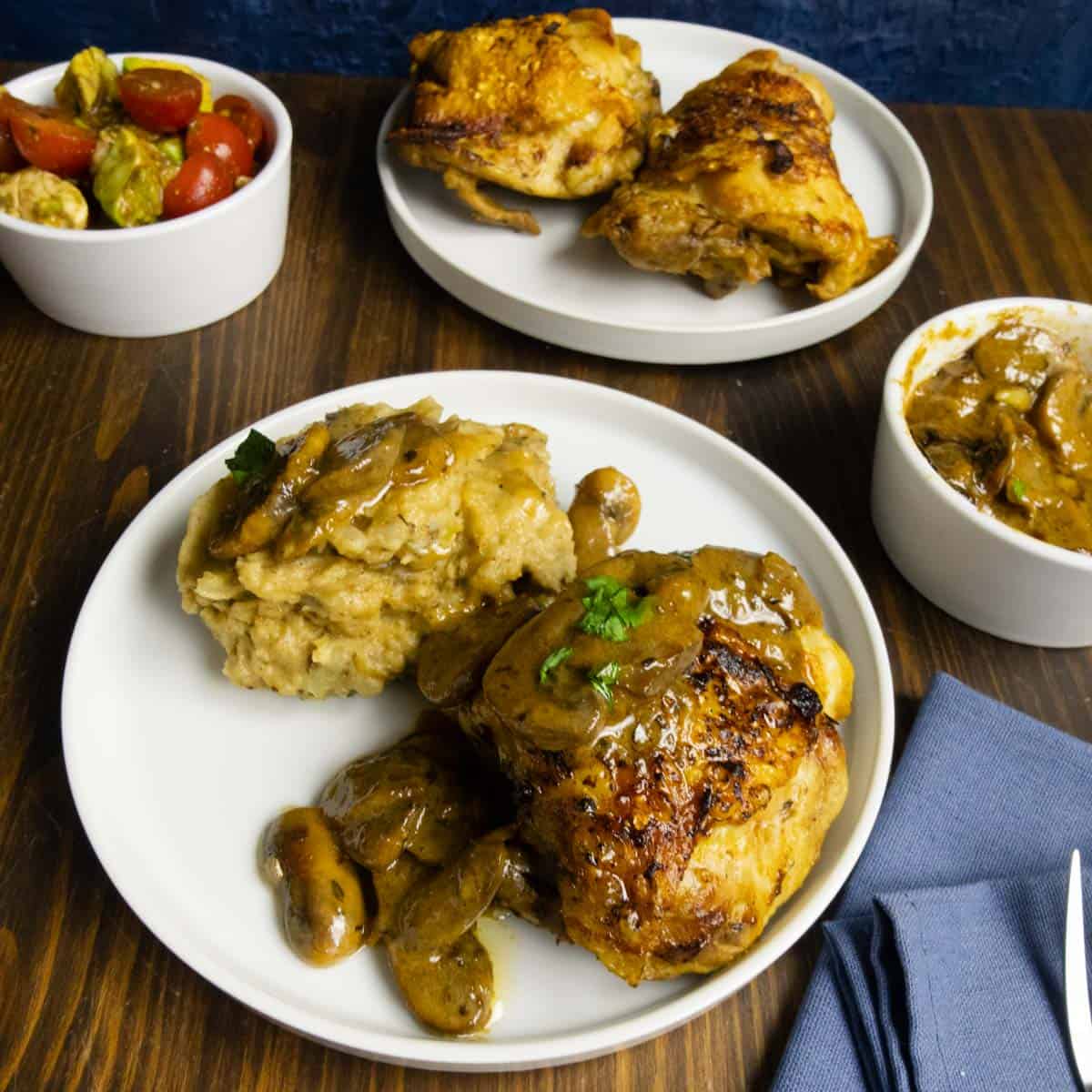 Chicken Marsala without wine on a plate with black garlic mashed potatoes with a tomato, avocado, mozzarella salad in the back.