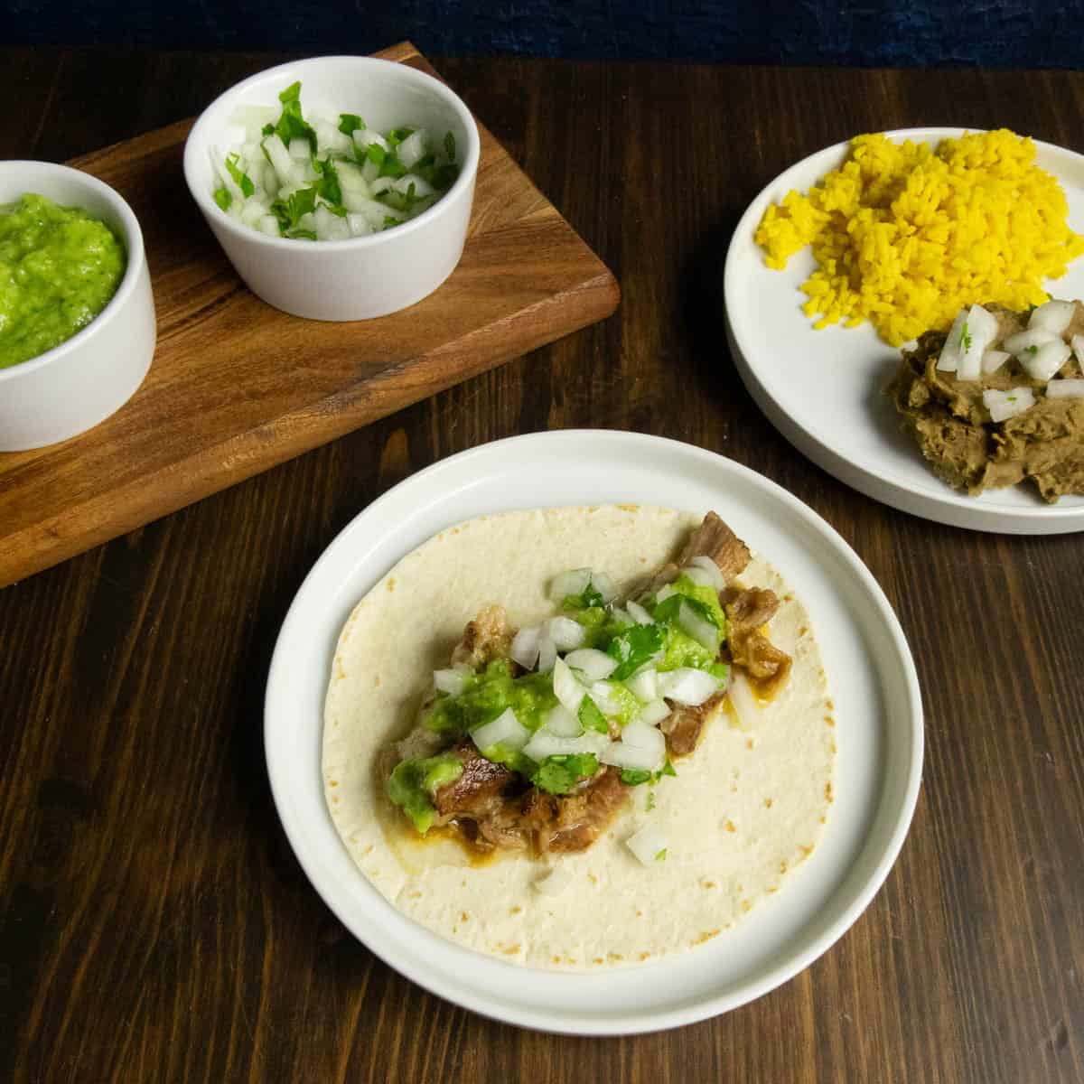 A plate with a Mexican Coke braised carnitas taco with yellow rice refried beans, and sauces in the background.