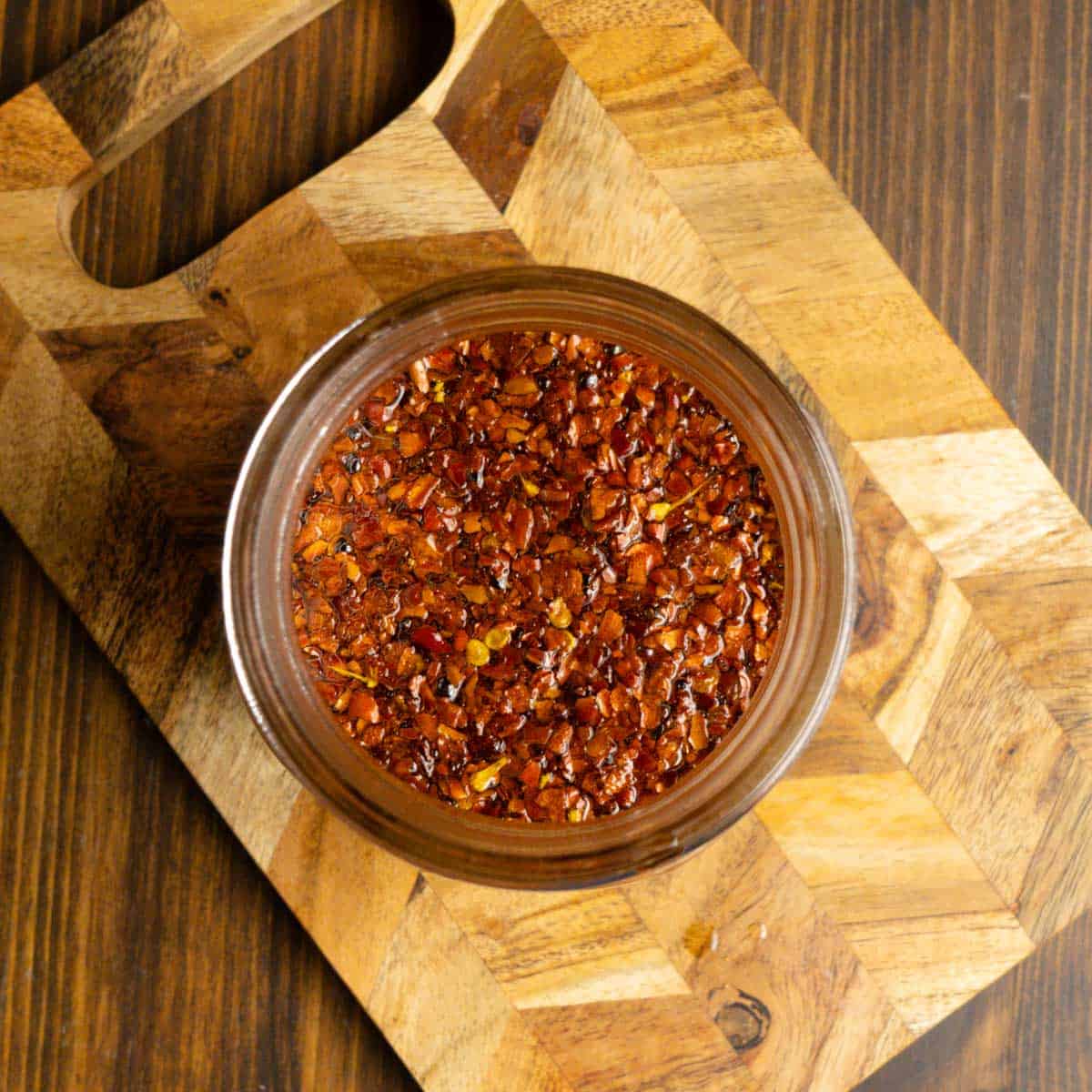 Close up of chili oil in a small mason jar on a cutting board.