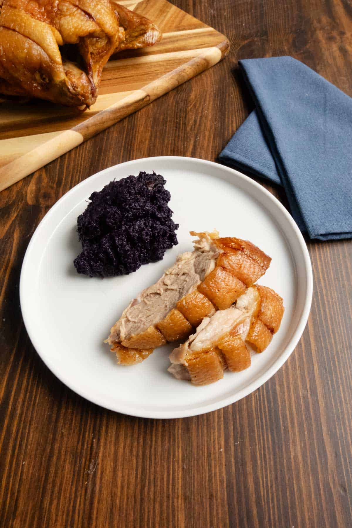 Sliced duck breast on a plate with purple sweet potatoes and a whole duck in the background.