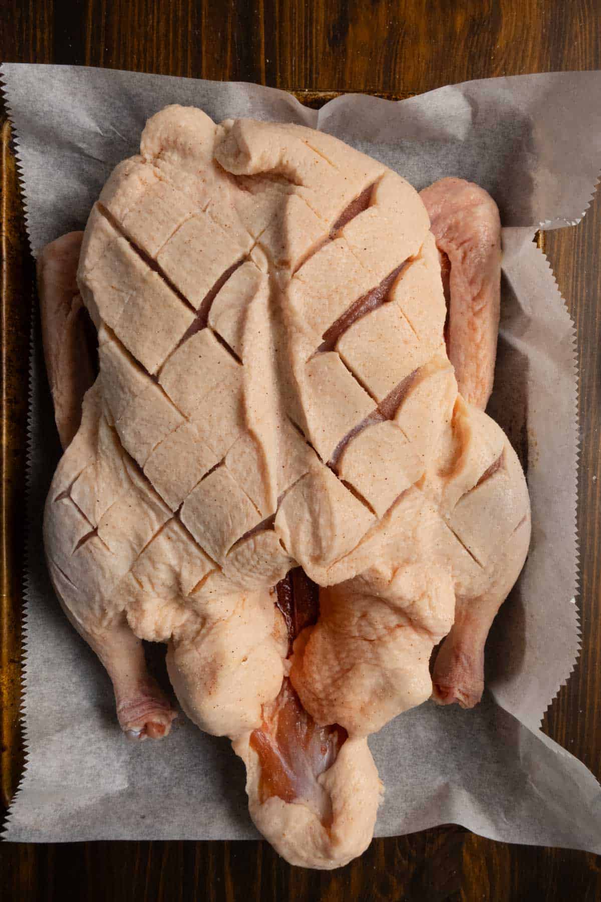 A whole duck on a baking sheet with cuts diagonally through it the other direction.