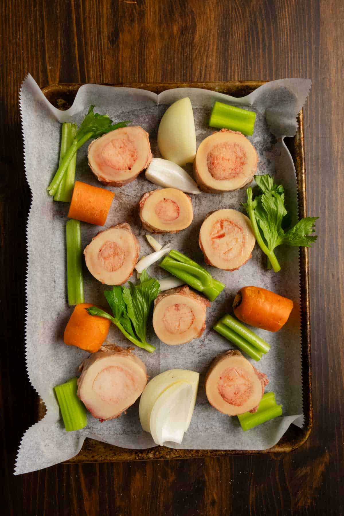 Beef marrow bones and vegetables on a sheet pan before roasting.
