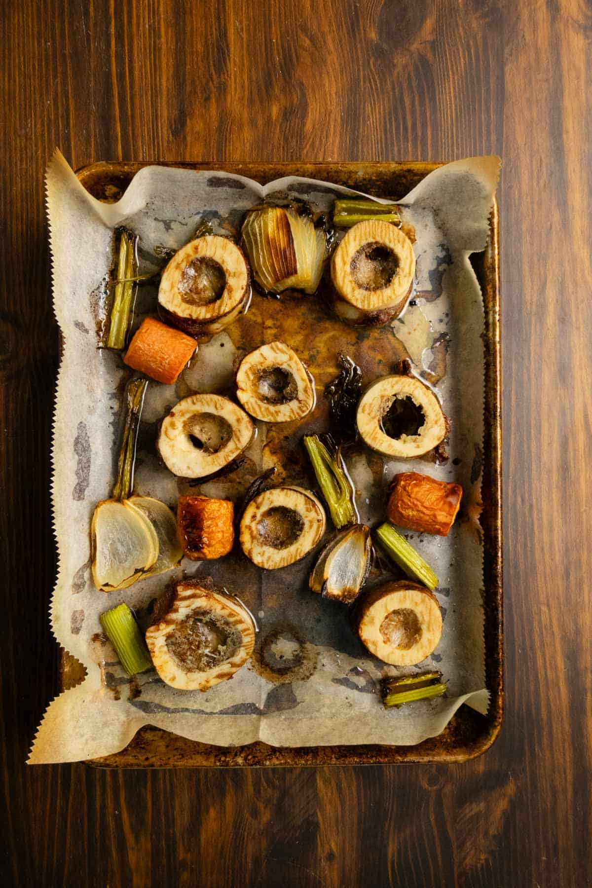 Beef marrow bones and vegetables on a sheet pan after roasting.