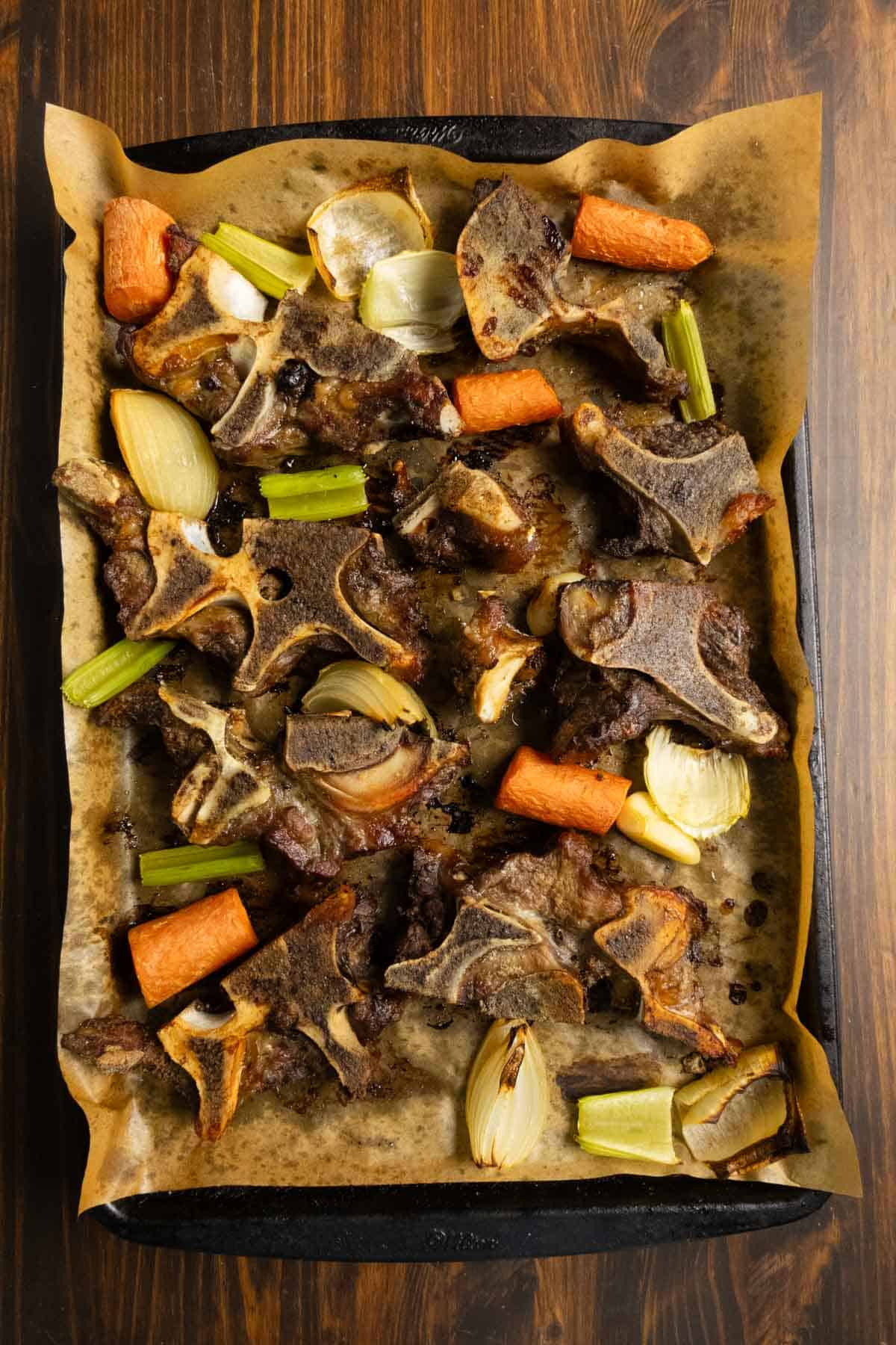 Beef neck bones and vegetables on a sheet pan after roasting.