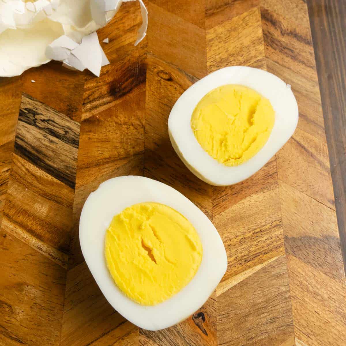 A perfectly cooked hard boiled egg cut in half on a cutting board with the shell off to the side.