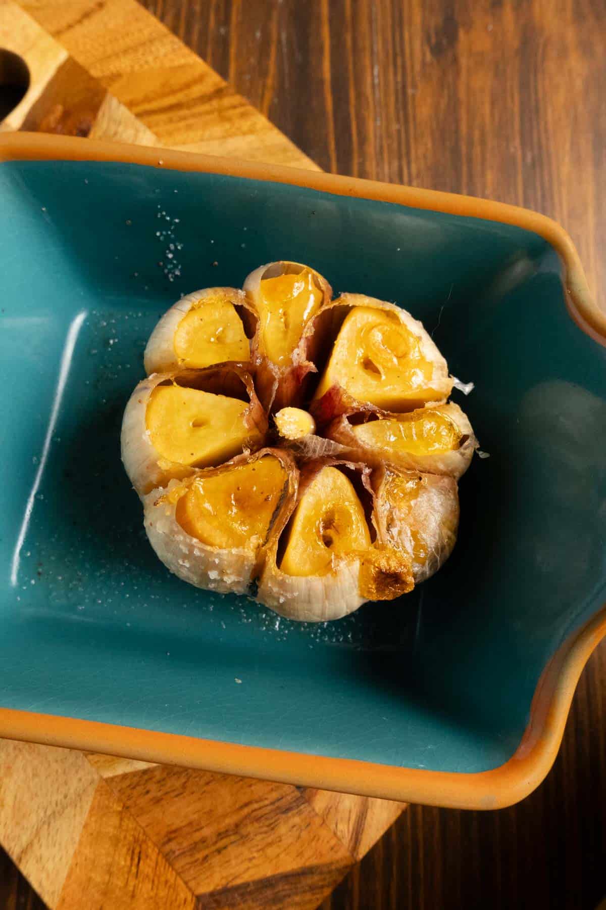 Close up on a freshly roasted garlic bulb in a blue baking dish.