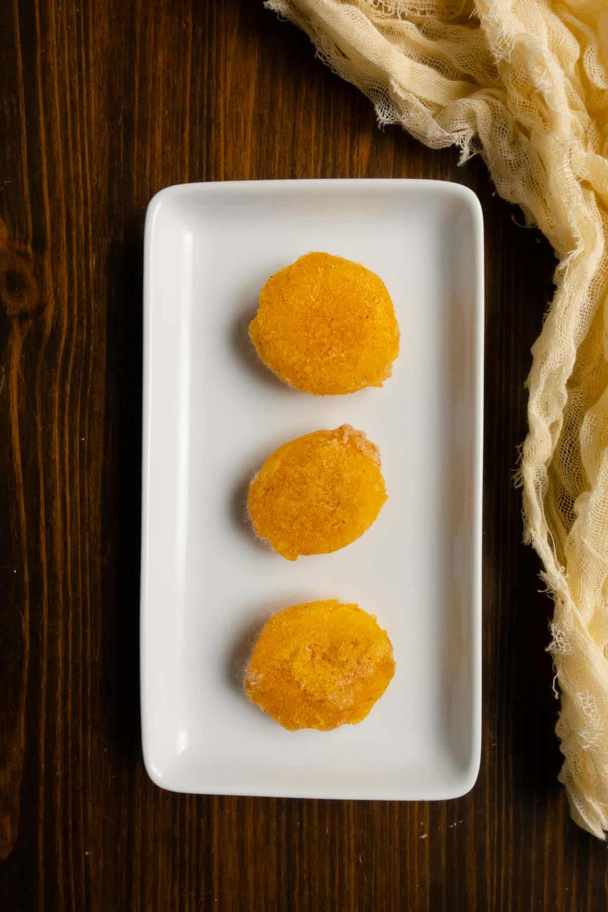 Three salt cured egg yolks on a white platter with cheesecloth in the background.