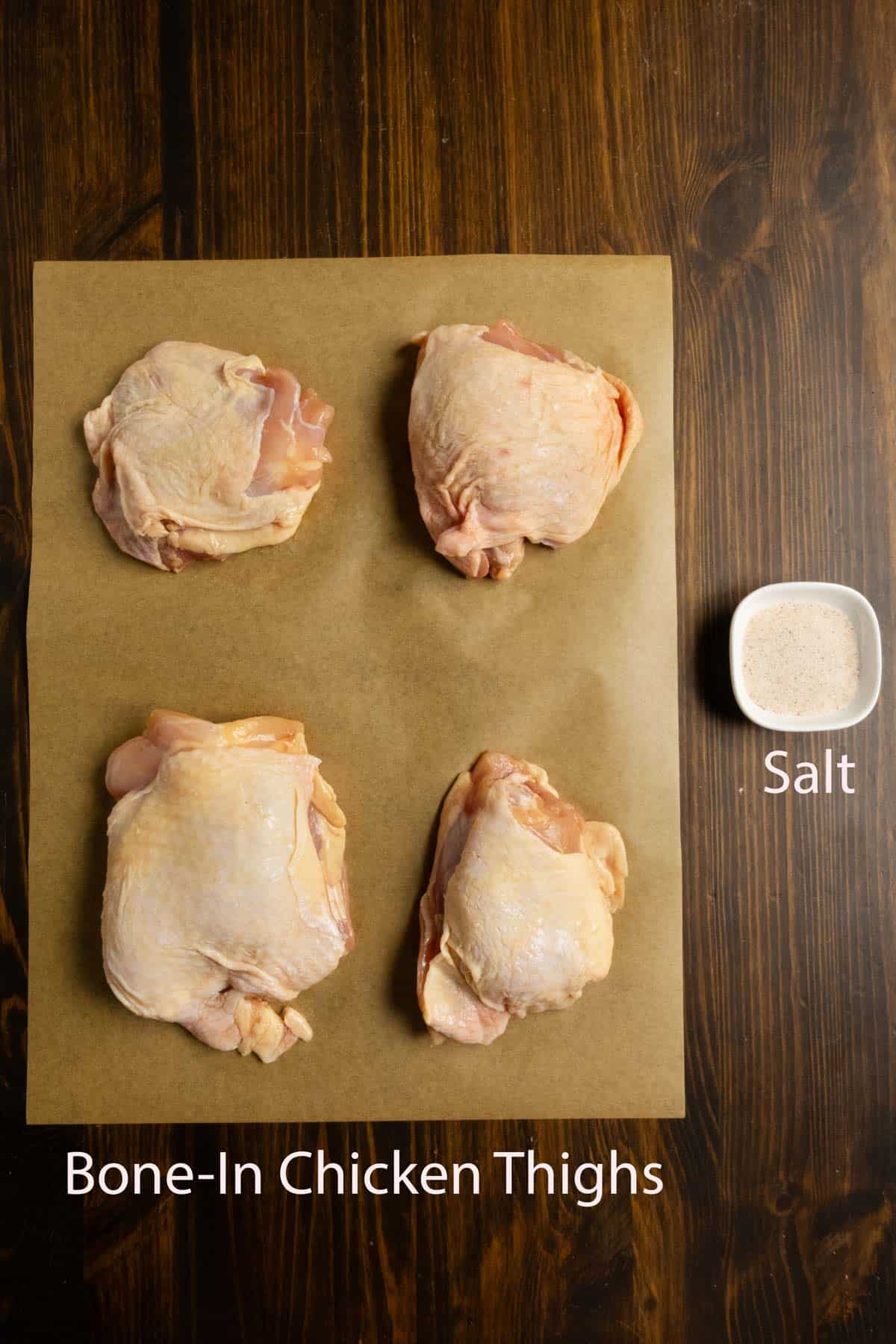 Chicken thighs on parchment paper with salt on the side.