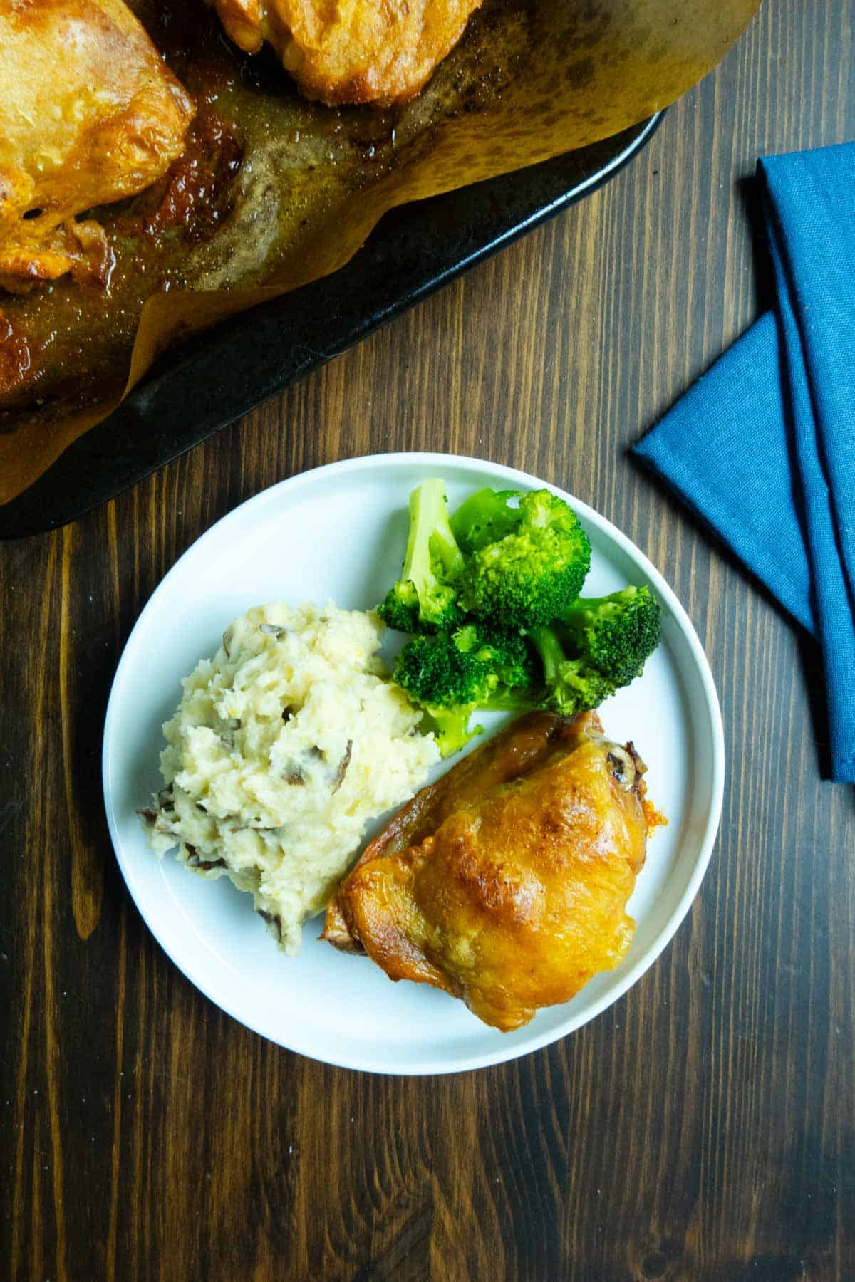 A crispy dry brined chicken thigh on a plate with broccoli and mashed potatoes.