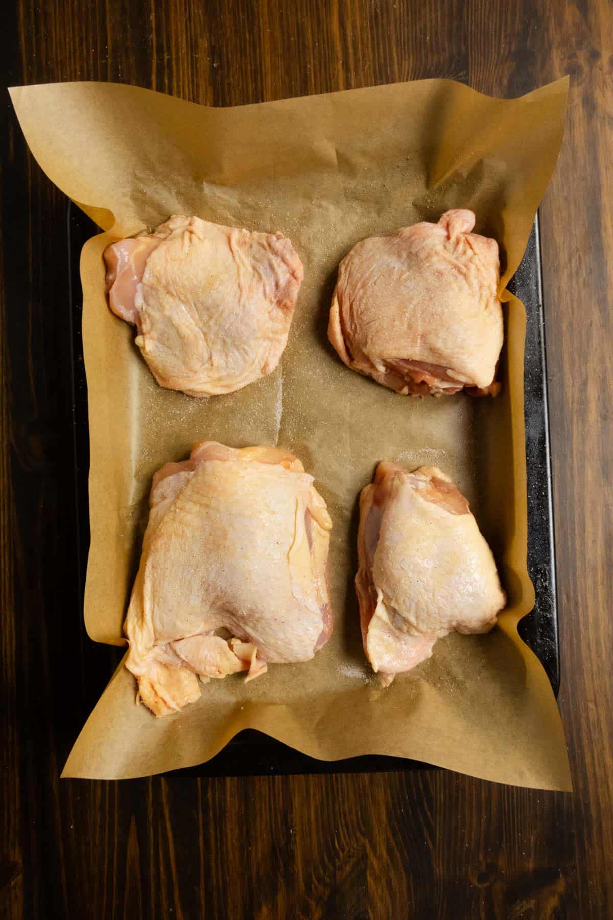 Chicken thighs on a tray with salt.