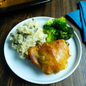 Crispy dry brined chicken thigh on a white plate with mashed potatoes and broccoli.
